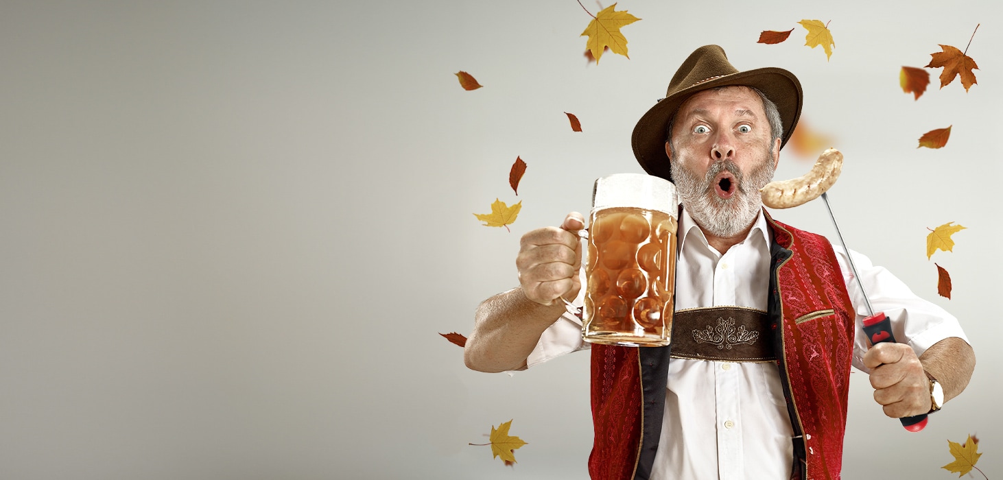 uomo con in mano un boccale di birra e un cacciavite che infilza un weisswurst. Sfondo di foglie autunnali.